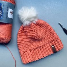 an orange knitted hat next to a ball of yarn and a crochet hook