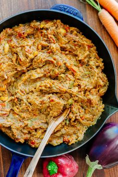 a pan filled with food sitting on top of a wooden table next to carrots