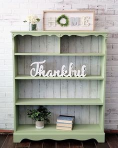 a green bookcase with the words thank you're home on it and a potted plant next to it