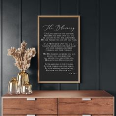 a wooden dresser with two vases and a framed poem on the wall above it