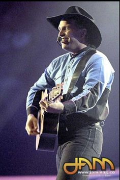 a man wearing a cowboy hat and holding a guitar in his right hand while standing on stage