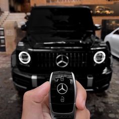 a hand holding a remote control in front of a black mercedes benz suv parked on the street