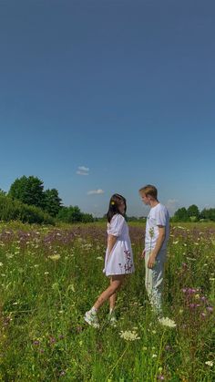 a man and woman standing in a field with wildflowers under a blue sky