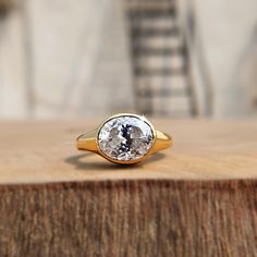 a gold ring with an oval cut diamond on it sitting on top of a piece of wood