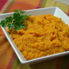 a white bowl filled with mashed carrots and garnished with parsley