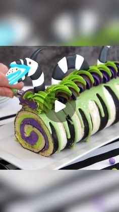 a person cutting into a cake with green and purple icing on top of it