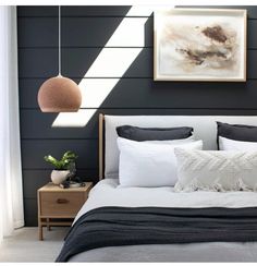 a bed with black and white sheets, pillows and a painting on the wall above it