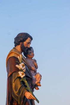 a statue of jesus holding a child in his arms, with the sky behind him