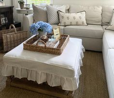 a living room with white couches and blue flowers in a basket on the coffee table