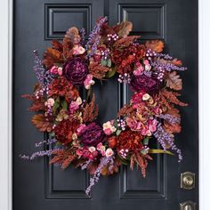 a wreath on the front door with purple and red flowers hanging from it's side