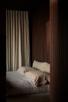 an unmade bed in a dark room with curtains on either side and light coming through the window