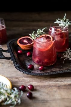 three glasses filled with blood oranges and rosemary garnish on a black tray