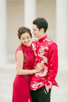 a man and woman standing next to each other in front of some columns wearing red outfits