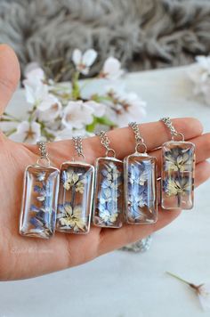 four glass pendants with flowers in them on a person's hand next to some flowers