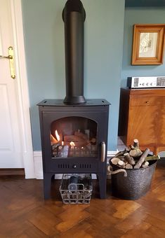 a wood burning stove sitting on top of a hard wood floor next to a basket filled with logs