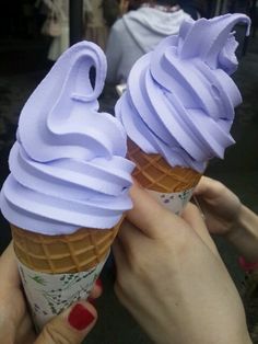 two ice cream cones with purple icing on top are being held up by someone's hands