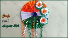 an orange, white and green fan with flowers hanging from it's side on a marble surface