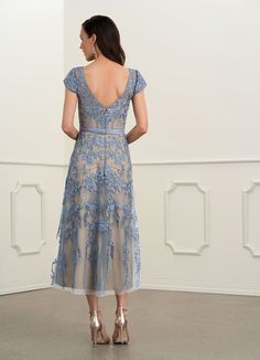 a woman in a blue dress is looking at the wall with her back to the camera