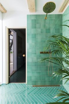 a green tiled shower in a bathroom next to a potted plant