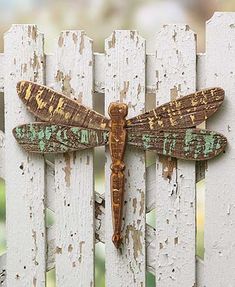 a wooden dragonfly sitting on top of a white fence