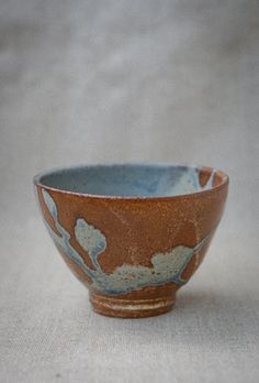 a brown and blue bowl sitting on top of a white cloth covered table next to a wall