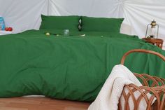 a bed with green sheets and pillows next to a wicker basket on the floor