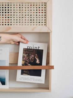 a person's hand is reaching for some books on a book shelf in front of a white wall