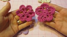 two crocheted flowers being held by someone's hands on top of a table