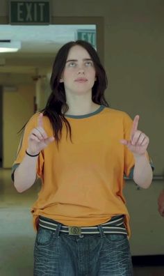 a woman in an orange shirt is holding her hands up and making the peace sign