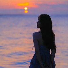 a woman standing in front of the ocean at sunset