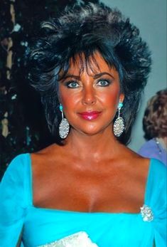 a woman in a blue dress posing for the camera with big earrings on her head