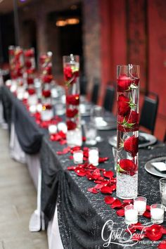 the table is set up with red roses and candles in tall vases on each side