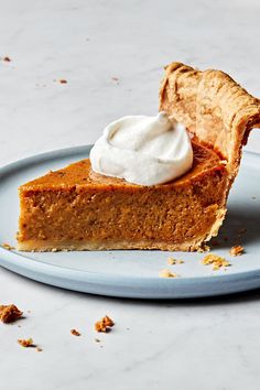 a slice of pumpkin pie with whipped cream on top sits on a blue and white plate