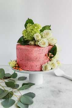 a pink cake with white flowers and greenery on top