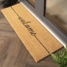 a welcome mat with the word welcome on it next to a potted green plant