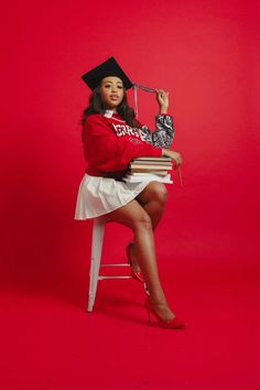 a woman sitting on top of a stool with books in her hand and wearing a graduation hat