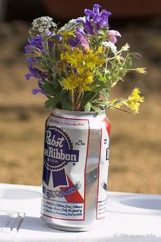 an image of a beer can with flowers in it on the table next to a photo of a bride and groom