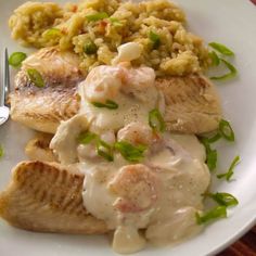 a white plate topped with fish covered in gravy next to rice and a fork