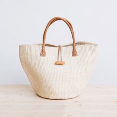 Rural Kamba women in Kenya hand-weave these beautiful handbags from tough sisal fibers. Sisal grows well in the semi-arid climate of eastern Kenya, and its spiky leaves contain long fibers that can be extracted for weaving.  approximate size: 10" diameter x 10" tall (without handle), 17" tall (with handle) leather hand Natural Basket-shaped Handwoven Beach Bag, Natural Handwoven Basket Beach Bag, Daily Use Handwoven Burlap Straw Bag, Daily Handwoven Burlap Straw Bag, Eco-friendly Natural Straw Market Bag, Handwoven Cream Straw Bag For Everyday Use, Cream Handwoven Straw Bag For Everyday Use, Beige Handwoven Burlap Straw Bag, Beige Woven Burlap Straw Bag