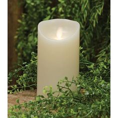 a white candle sitting on top of a wooden table next to green leaves and bushes