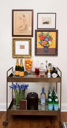 a bar cart with drinks and flowers on it in front of two framed art pieces