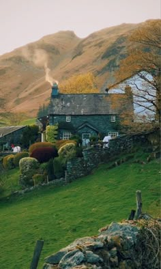 a house in the middle of a lush green field with mountains in the back ground