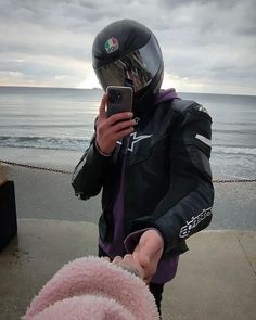 a person wearing a motorcycle helmet and holding a cell phone near the ocean on a cloudy day