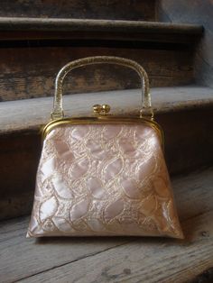 "This is a plastic covered gold and beige brocade purse from the 1950's or early 1960's. It features a gold confetti lucite handle. The gold tone kiss clasp works well. It has a peach pink sateen lined interior. No rips, tears, dirt to tell of. This purse is in great shape! Comes from a smoke free home. Measurements: Length: Bottom: 10\" top: 8\" Height without Handle: 8.5\" with Handle: 12\" Width at Bottom: 3\" Please ask me any questions you may have before buying as this is a final sale. Ple Vintage Gold Embroidered Evening Bag, Gold Vintage Embroidered Evening Bag, Vintage Embroidered Evening Bag For Party, Vintage Beige Evening Bag For Party, Vintage Wedding Bags With Gold Embroidery, Vintage Beige Evening Bag Gift, Vintage Beige Evening Bag For Gift, Vintage Beige Evening Bag For Wedding, Vintage Beige Evening Bag For Events