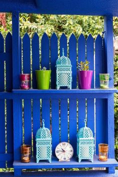 a blue shelf with pots, cups and a clock sitting on it's side