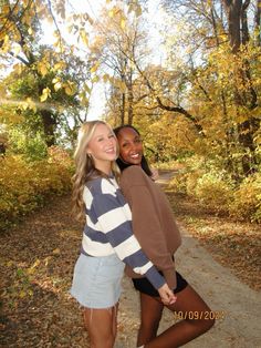 two young women standing next to each other on a path in the woods with autumn leaves