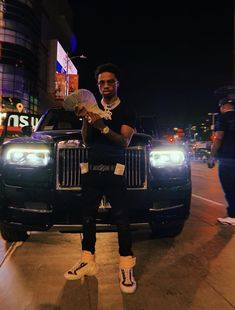 a man sitting on the hood of a black car in front of a building at night