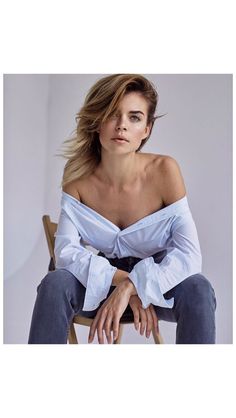 a woman sitting on top of a wooden chair wearing a white shirt and blue jeans