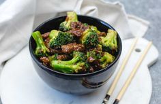 a bowl filled with beef and broccoli next to chopsticks