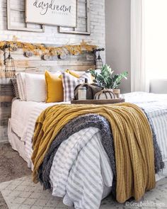 a bed with yellow and gray blankets on it in front of a white brick wall